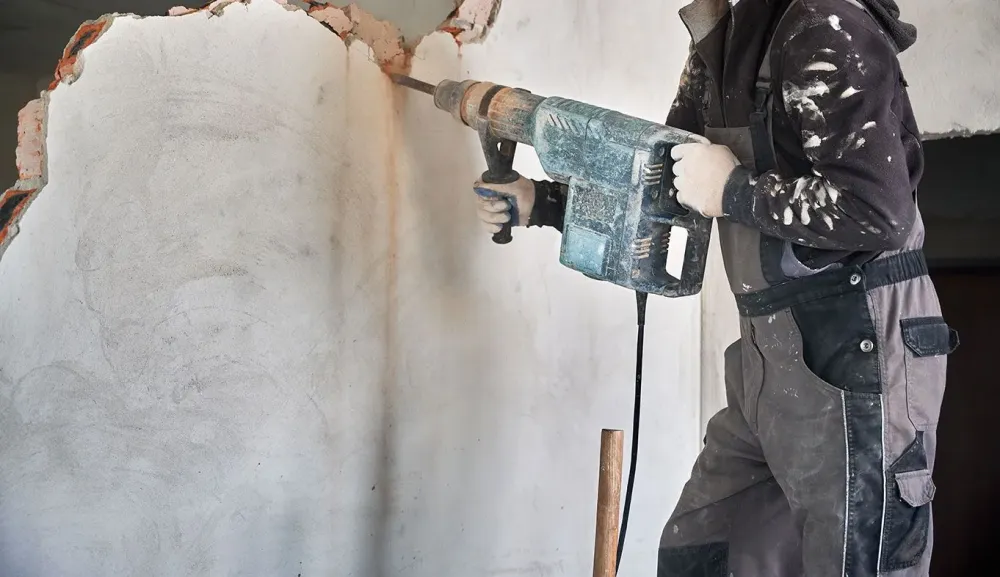 Homme-qui-utilise-une-perçeuse-à-percussion-pour-creuser-dans-un-mûr-100webp